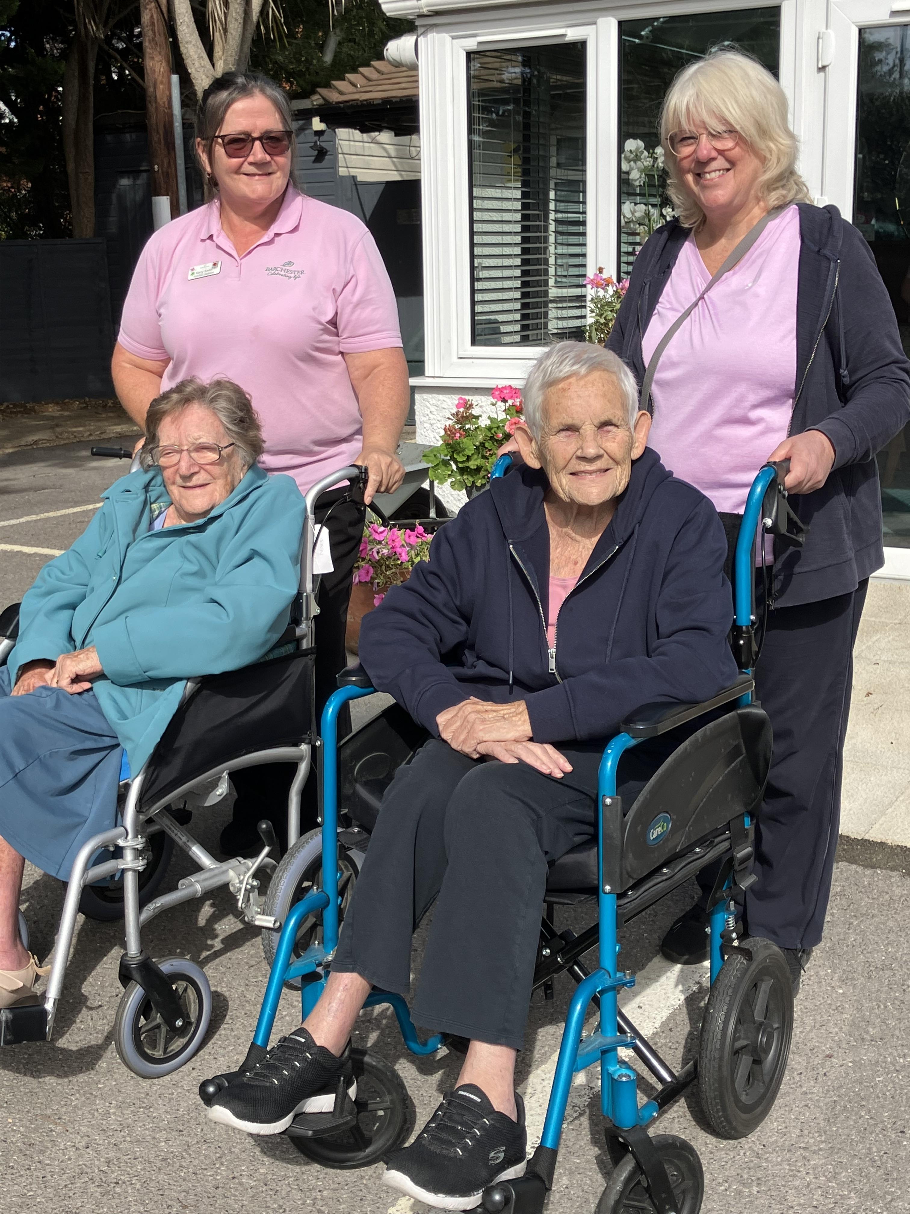 Two happy residents in wheelchairs, supported by the 2 activities team members.