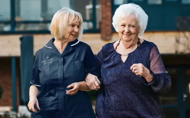 A nurse walking outdoors with a resident