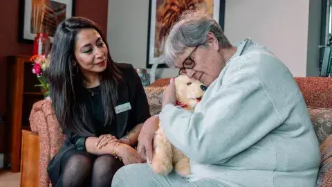 Care home manager comforting a dementia resident with a robotic therapy dog in a lounge